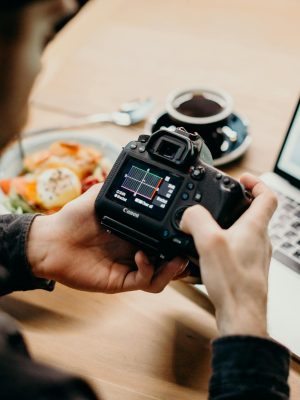 A man reviews photo settings on a camera while working on a laptop in a cozy workspace.