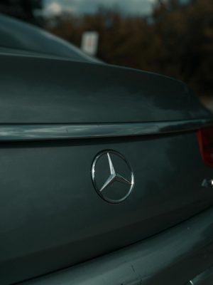 Close-up of Mercedes-Benz emblem on a luxury car's rear, surface details highlighted in natural light.