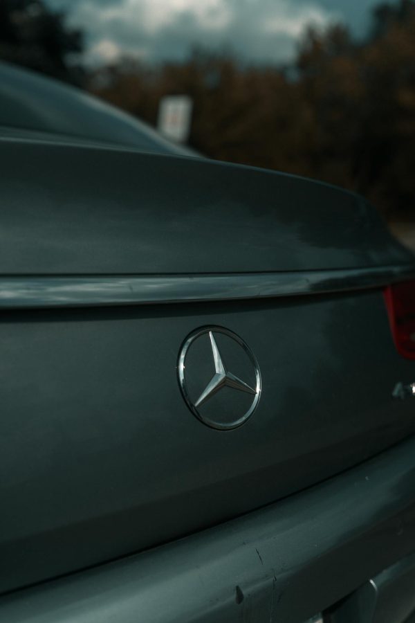 Close-up of Mercedes-Benz emblem on a luxury car's rear, surface details highlighted in natural light.