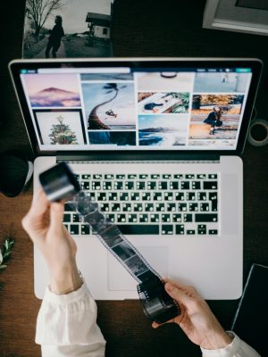 Person holding film strip over laptop showcasing photography work.